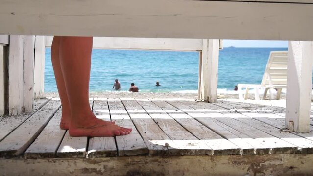 Woman in the changing, dressing room on beach, at sunset on the seashore. Close-up of bare female feet legs in enclosed changing room cabin. Summer holiday vacation and travel concept. Slow motion
