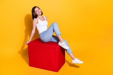 Obraz premium Full length photo of sweet adorable woman wear white singlet sitting red cube empty space isolated yellow color background