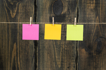 Clothespins with blank notepaper on twine against wooden background space for text. note blank color paper cards on rope against wooden board. blanks for designers