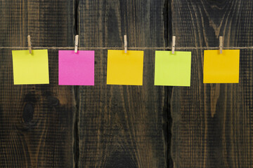 Clothespins with blank notepaper on twine against wooden background space for text. note blank color paper cards on rope against wooden board. blanks for designers