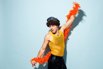 Side view young fun happy gay Latin man wears mesh tank top hat yellow clothes tinsel dance isolated on plain pastel light blue cyan background studio portrait. Pride day June month love LGBT concept.