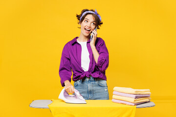 Young happy smiling woman wear casual purple shirt do housework tidy up ironing clean clothes on...