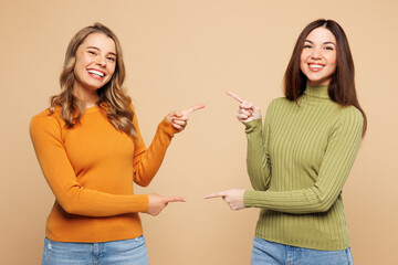 Young friends two women they wears orange green shirt casual clothes together point finger on each other, area between them isolated on plain pastel light beige background studio. Lifestyle concept. - 775737896