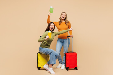 Young friends two women wearing orange green shirt together hold passport ticket sit on bag...