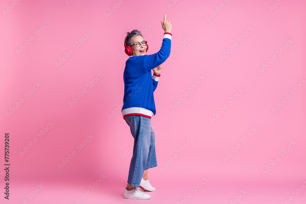 Poster Photo of excited old lady listen headset playlist dance isolated over pastel color background