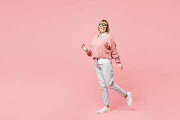 Full body side profile view fun elderly woman 50s years old wear sweater shirt casual clothes glasses walking going isolated on plain pastel light pink background studio portrait. Lifestyle concept.