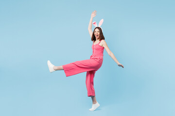 Full length body side view young funny woman wear pink casual clothes rabbit bunny ears raise up leg hand dance stand on toes isolated on plain blue background studio. Lifestyle Happy Easter concept.