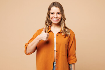 Young smiling happy Caucasian woman she wear orange shirt casual clothes showing thumb up like gesture look camera isolated on plain pastel light beige background studio portrait. Lifestyle concept.