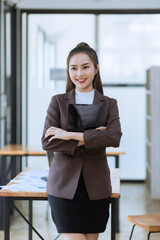 Asian businesswoman standing with arms crossed and tablet in office.