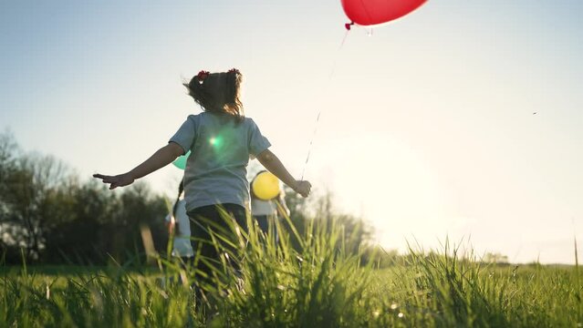 Child birthday. Girls and boy play in park at sunset in grass. Family run with balloons. Happy cheerful children outdoors in field. Summer in park smile children with balloons. Happy childhood concept