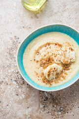 Turquoise bowl with roasted cauliflower cream-soup, vertical shot on a beige granite surface, high angle view with space