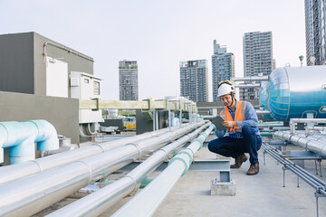 engineer male technician worker working service hotel boiler tank hot water supply pipe system. man safety checking maintenance pipeline heating water delivery line at roof top outdoor.