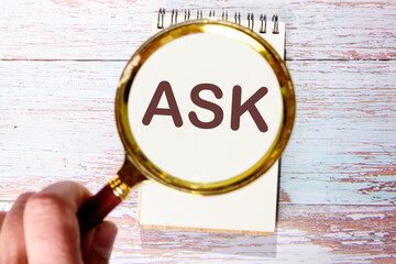 Business concept. The word ASK is written through a magnifying glass in a notebook against the background of old boards