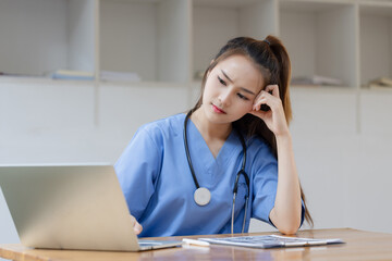 Asian female doctor with blue coat is stressed and tired from work on desk in hospital.