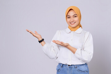 Happy Asian Muslim woman showing copy space on palm isolated on white background. Ramadan and Eid Fitr celebration concept