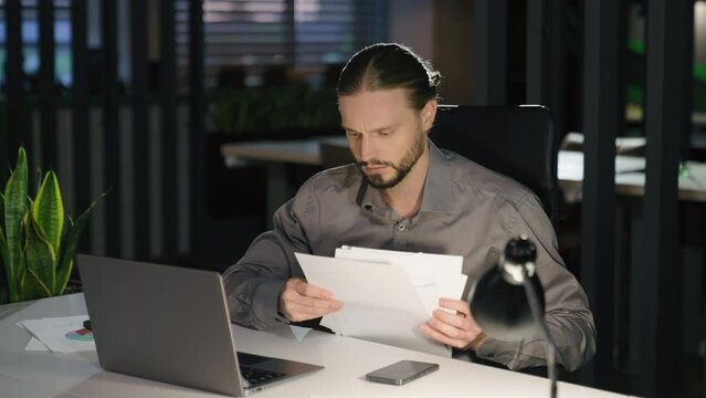 Stressed worried Caucasian tired exhausted man business problem male guy worker check data in papers documents and laptop businessman busy with computer paperwork managing in dark office night stress