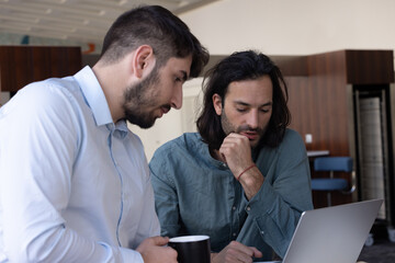 deux collègues, jeunes employés de bureau travaillent en équipe et discutent assis devant un ordinateur portable - 775758028