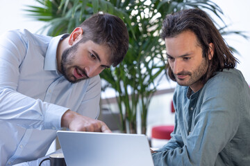 deux collègues, jeunes employés de bureau travaillent en équipe et discutent assis devant un ordinateur portable
