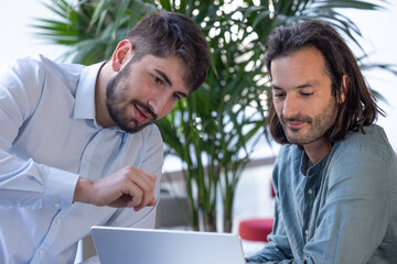 deux collègues, jeunes employés de bureau travaillent en équipe et discutent assis devant un ordinateur portable - 775758254