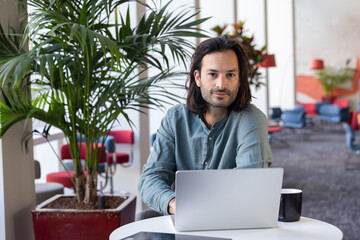 portrait d'un employé de bureau, homme d'affaires sympathique assis qui travaille avec un ordinateur portable. Il regarde la caméra en souriant - 775758475