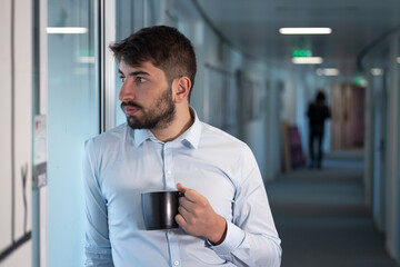 portrait d'un jeune homme employé de bureau ou homme d'affaires pensif qui fait une pause en buvant un café debout dans les couloirs de son entreprise