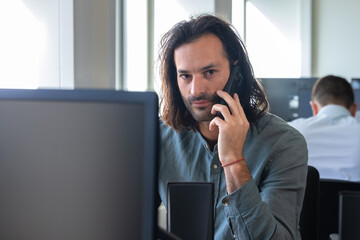Homme, employé de bureau, salarié d'une entreprise qui travaille devant un ordinateur. Il parle au téléphone - 775759209