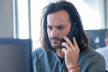 Homme, employé de bureau, salarié d'une entreprise qui travaille devant un ordinateur. Il parle au téléphone - 775759247