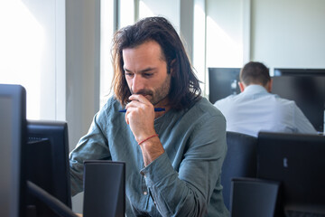 Portrait d'un bel homme de 30 ans qui travaille dans un bureau. il a les cheveux longs et une barbe - 775759292