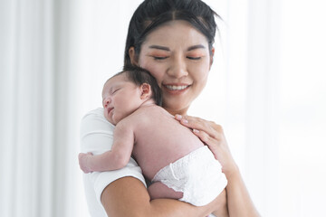 Mother carrying her newborn baby girl on shoulder at home. Cute 19 days Asian Australian infant baby sleeping in mom arms. Parent and little kid relaxing together. Selective focus on child