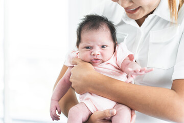 Smiling mother carrying of her newborn baby girl at home. Cute 19 days Asian Australian infant baby...