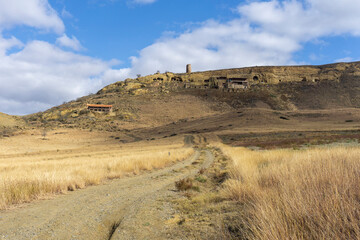 An earthen road through the savanna leads to the monastery on the hill. Dried orange grass. Bright...