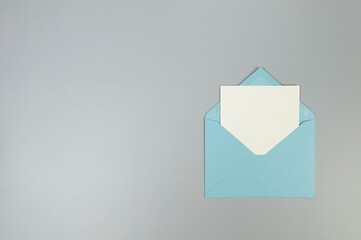 Top view of blue envelope, white card on grey background. Post flat lay. Copy space.