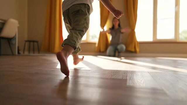 Happy family. Baby feet walk on floor towards mother. Child makes steps barefoot on parquet floor in children room. Son runs to his mother on the laminate with his bare feet. happy baby first steps