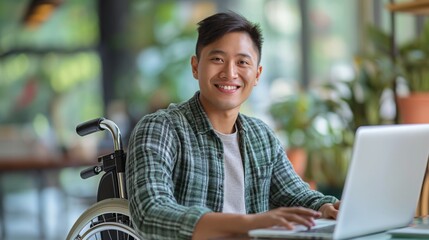 Happy asian young man in wheelchair at desk working on laptop. Disabled person without the ability to move independently. Concept inclusivity at workplace, digital nomad, online education.
