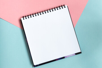 Top view of open notebook with clean sheet. Template for message. Empty spiral sketchbook with white paper on pastel pink and blue background.  - obrazy, fototapety, plakaty