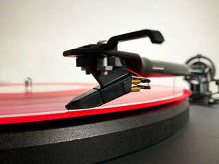 Macro closeup of a pink or red vinyl LP record on a turntable, with the tonearm needle or stylus...