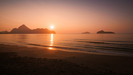 Orange sun dips below the horizon, painting the sky and ocean in fiery hues of red and gold