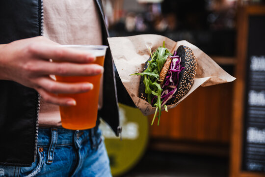 Close up of woman hands holding delicious organic salmon vegetarian burger and homebrewed IPA beer on open air beer an burger urban street food festival in Ljubljana, Slovenia