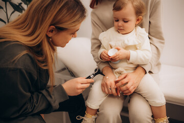 Child with teddy bear getting ENT examination in exam room at medical checkup at doctor's office. Female otolaryngologist holding otoscope and examining little kid's ear to prescribe the right therapy - obrazy, fototapety, plakaty