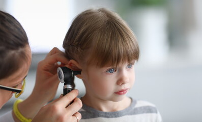 Otorhinolaryngologist examines little girl's ear with otoscope. Adenoiditis as cause of otitis media in children concept. - obrazy, fototapety, plakaty