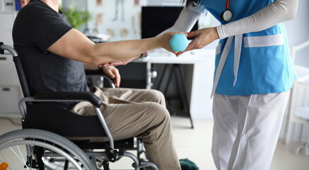 Female nurse helps lift dumbbell to disabled patient rehabilitation therapy concept. Process of recovering patients after severe injuries