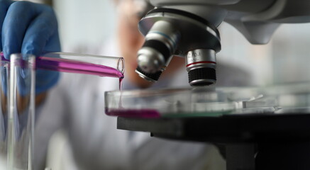 Close-up of lab assistant hand holding test-tube. Scientist adding reagent in container. Chemist...