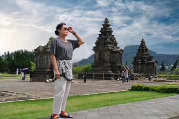 A woman, wearing sunglasses, is enjoying the view around the Arjuna Temple compound in Dieng,...