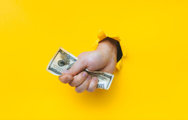 A right man's hand holds dirty money through a torn hole in yellow paper. Concept of dishonest...