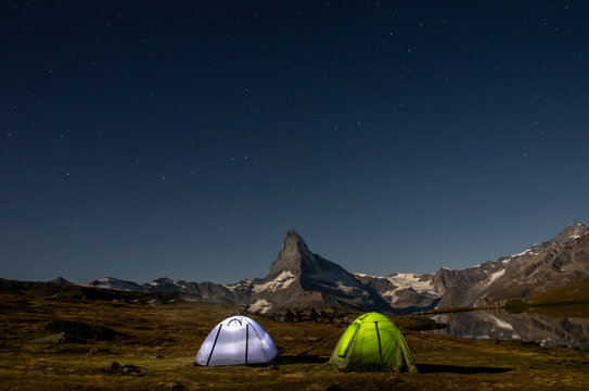 Two vibrant tents pitched beside Stellisee Lake at 2600 meters under a star-studded sky with the Matterhorn in Switzerland standing majestic in the background