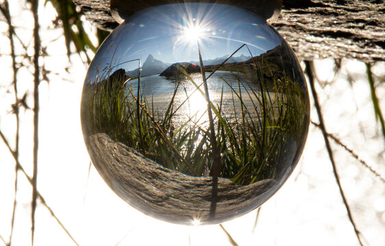 The Matterhorn mountain and surrounding landscape are beautifully captured within a crystal ball under the radiant sun, creating an enchanting inverted image