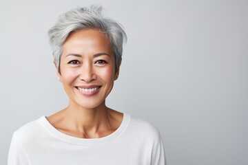 A woman with a short gray hair is smiling and wearing a white shirt