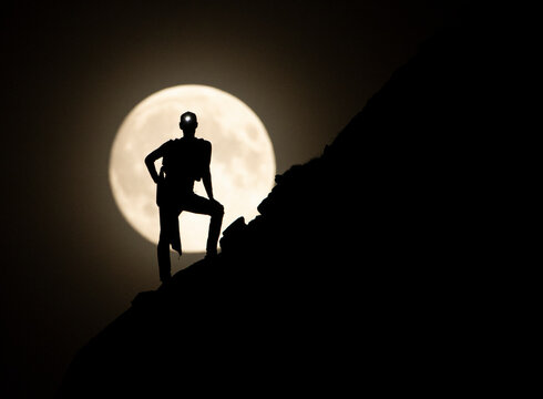 The silhouette of a climber is dramatically outlined against the backdrop of a brilliant full moon on a clear night, capturing the spirit of exploration