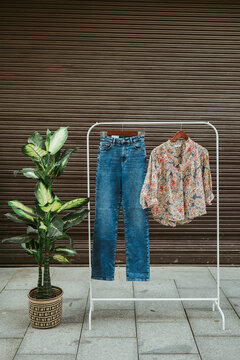A trendy fashion display pairs classic blue jeans with a vibrant patterned shirt, set against an urban backdrop with green foliage