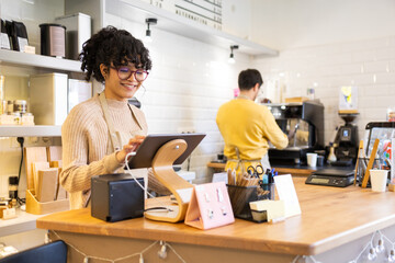 Cheerful hispanic woman barista using digital tablet at coffee shop counter